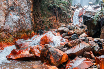 A scenic sulfur-rich stream with orange rocks and a waterfall in tropical nature. Perfect for concepts of geology, volcanic activity, hot spring, minerals, and natural landscape.
