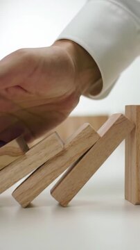 An elegant hand in professional attire initiates and swiftly halts a cascading line of light-colored polished wooden domino blocks on a pristine, modern surface with professional studio lighting and