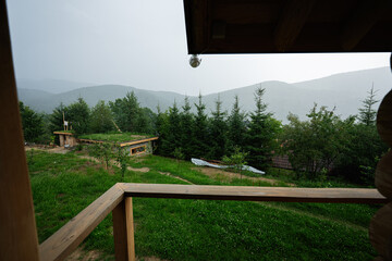 View from a wooden balcony overlooking lush greenery and distant hills on a misty day