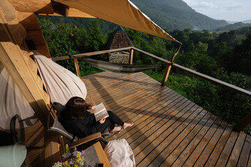 Woman reading a book on a wooden balcony overlooking a lush forest