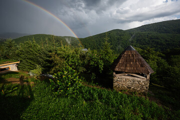 Rustic hut and rainbow in lush green countryside under moody sky