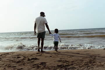 Father and son holding hands walking on beach enjoying vacation