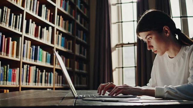 Young woman focused on laptop in cozy library sunlight