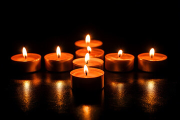 Several candles arranged neatly in the shape of a cross on a dark surface, representing prayer, remembrance, and faith