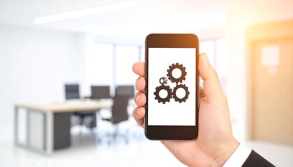 Hand holding smartphone displaying gear icon, blurred office background