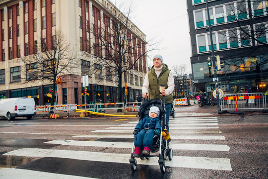 Chilly autumn city: dad pushes toddler stroller across wet streets, raw urban winter vibes, cold rainy day family moment.