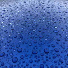 Water droplets on a smooth, vibrant blue surface. Close-up view of water beads on a vehicle's exterior.