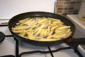 Freshly cut potato fries frying in hot oil inside a pan. Concept of homemade fast food, cooking at...
