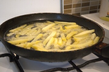 Freshly cut potato fries frying in hot oil inside a pan. Concept of homemade fast food, cooking at home, and comfort meals.