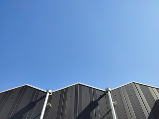 Fototapeta premium Modern Industrial Building Facade with Clear Blue Sky, A minimalist view of a modern industrial building facade under a clear blue sky. The image features geometric patterns, vertical lines