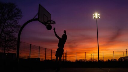 Man performing a powerful dunk at sunset on a basketball court