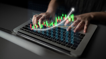 A close-up of hands typing on a laptop, accompanied by digital financial graphs. The image...