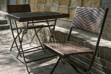 Wicker bistro set with folding table and chairs on an outdoor patio with stone wall backdrop
