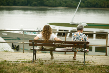 Two women sit on a riverside bench by the Danube in Ruse, Bulgaria, as a boat with a green deck...