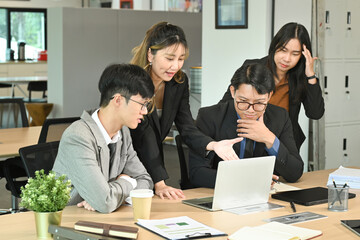 Group of business people working, the team are sitting at a board room table looking at a laptop...