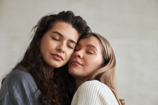 Close-up studio portrait of two beautiful lesbian women in love standing cheek to cheek with eyes closed