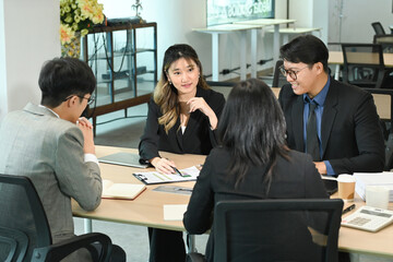 A group of people are sitting around a table in a business setting. They are all dressed in...