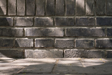 Textured dark gray brick wall with sunlight and shadows casting patterns on the surface