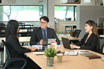 A group of people are sitting around a table in a business setting. One man is giving a presentation to the group, while the others listen intently.
