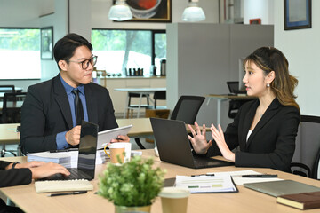 A group of people are sitting around a table in a business setting. They are all dressed in business attire and appear to be discussing something important