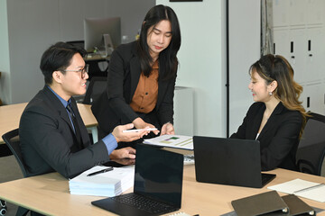 A group of people are sitting around a table in a business setting. They are all dressed in business attire and appear to be discussing something important