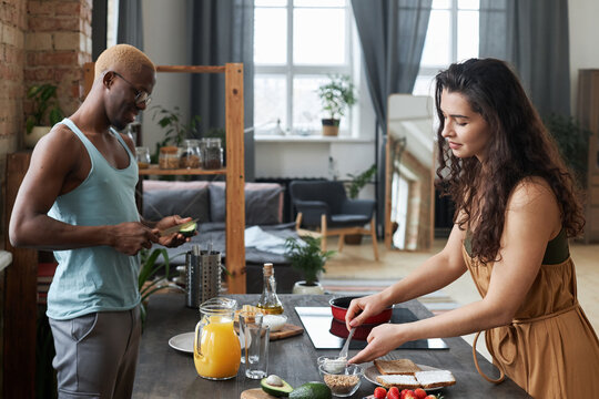 Horizontal medium portrait of modern ethnically diverse couple spending morning in kitchen cooking breakfast together
