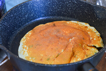 Pancake with fresh herbs frying in a pan, bubbles rising as it cooks. Ideal for food blogs, recipe...