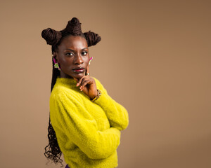 African woman in yellow sweater posing with hand on chin, confident studio portrait