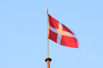 Danish flag is waiving on the wind against blue sky during sunset. 