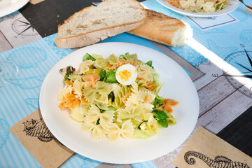 Colorful farfalle pasta salad with boiled egg and bread on nautical tablecloth