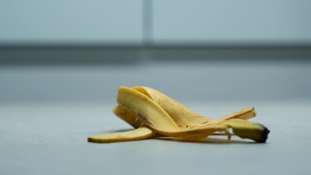 A banana peel lies on a ceramic kitchen tile.
Trash on the floor.
A discarded banana peel lies on the gray floor of the room.
Someone dropped a banana peel on the floor.