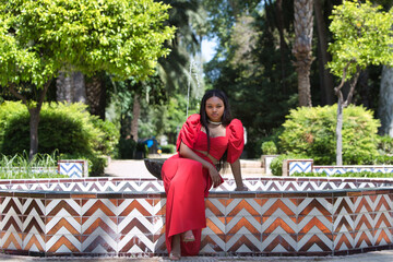 African woman, with long brown hair, young and beautiful dressed in an elegant red dress sitting...