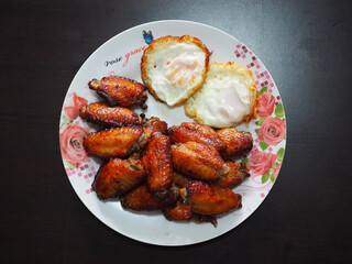 Glazed chicken wings and two fried eggs with runny yolks served on a floral plate, creating a rich, homemade protein-packed meal.