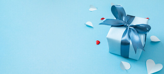 Festive composition with a blue gift and hearts on a pastel blue background.