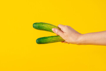Fresh green cucumber in hand on yellow background