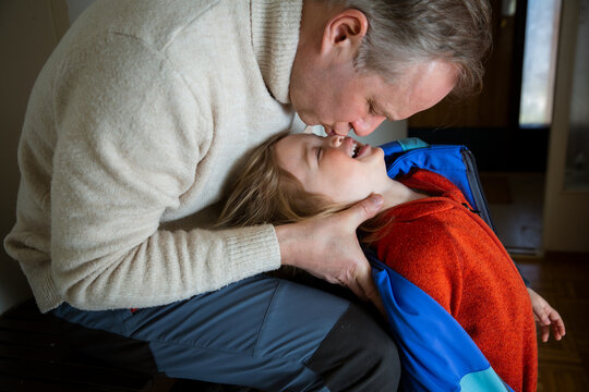 Father and toddler laughing and hugging in hallway during dressing, touching noses, tender family moment in cold season preparation.