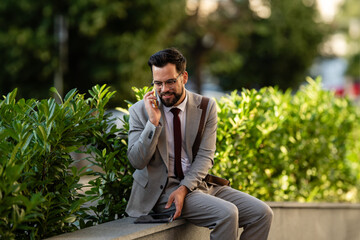 Businessman talking on phone while sitting on wall outdoors