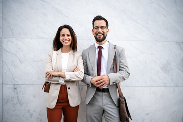 Smiling businesspeople standing with arms crossed in front of marble wall