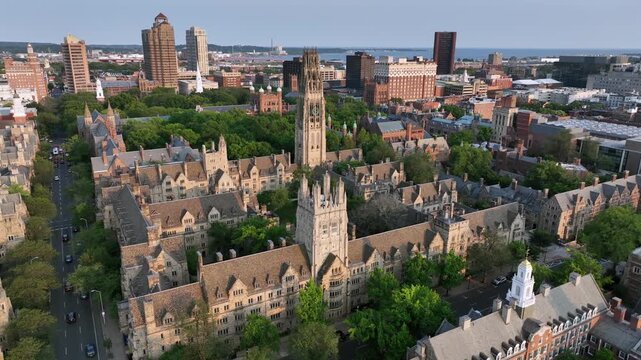Harkness Tower at Yale old campus university of New Haven. American City in Connecticut at sunrise. Summer day with green trees. Connecticut Financial Center In background. Aerial approaching shot.