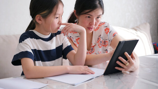 Mom explains to her daughter how to solve the problem. A woman and a girl are watching a lesson on a tablet. The child looks at the tablet