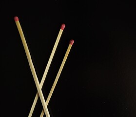 Two wooden matches with red tips intersect on a smooth black surface. The stark contrast highlights their shape and texture, creating a minimalist visual effect.