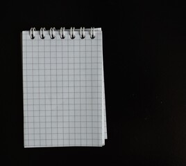 A blank graph paper notepad lies on a dark surface, inviting creativity with its grid layout. Ideal...