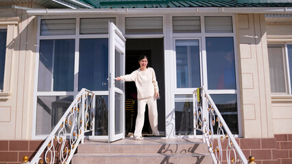 An Asian woman stands on the porch of a house with the door open and looks outside. The staff greets the guests. The hostess of the house opens the door