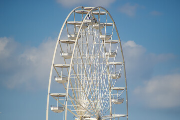 A towering white Ferris wheel stands against a bright blue sky dotted with clouds, showcasing...