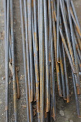 Close-up of rusty steel reinforcement bars (rebar) stacked on the ground at a construction site. The iron rods show corrosion and texture details, symbolizing building materials, heavy industry.