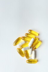 Various capsules in shades of yellow and white are scattered on a plain surface. This assortment represents dietary supplements promoting health and vitality.