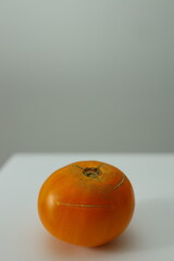 A ripe persimmon sits alone on a plain white surface, emphasizing its bright orange hue and unique...
