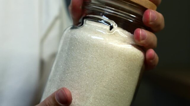 white loose sugar in a jar close-up.
Crystallized sugar in a container.
Calories and junk food.
Sweet food additive that is harmful to your health