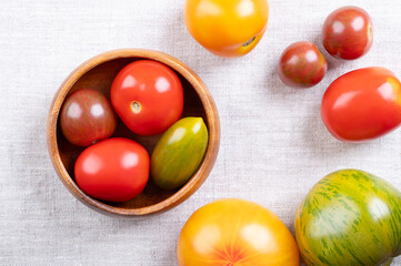 Fresh and ripe tomatoes of various varieties, colors, and sizes in a wooden bowl, on linen. Varieties of the plant Solanum lycopersicum, whose fruits are edible berries and are eaten as vegetables.