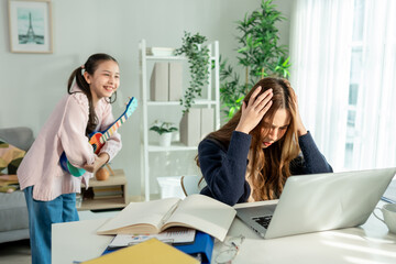 Asian mother work from home while playful daughter make noise beside her. 